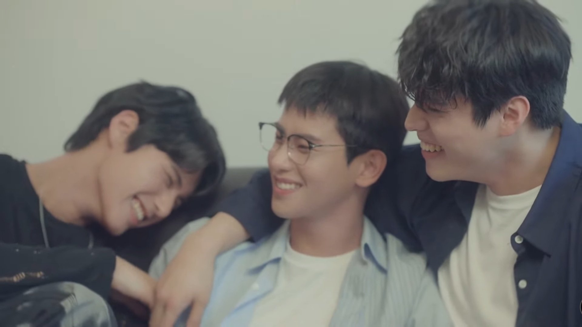 three men smile and laugh while sitting on a couch together in a still from the bl kdrama choco milk shake