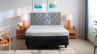 Best mattress in a box: The Layla Mattress in a box placed on a black bed frame and sat next to a wood and fabric chair