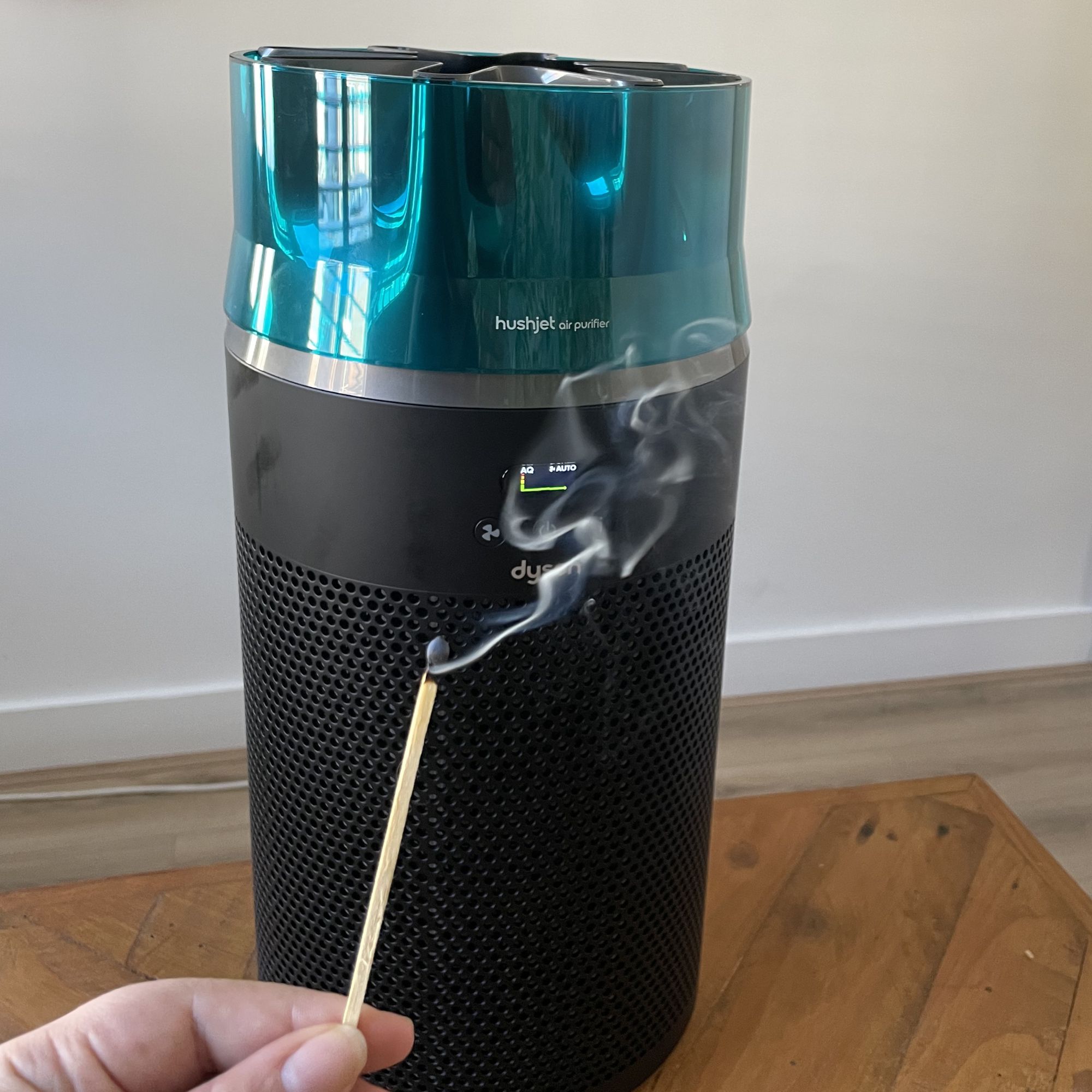 Hand holding a burnt match with smoke coming off it in front of the Dyson Hushjet Air Purifier