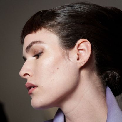 model backstage with her face side on with clear, glowy skin