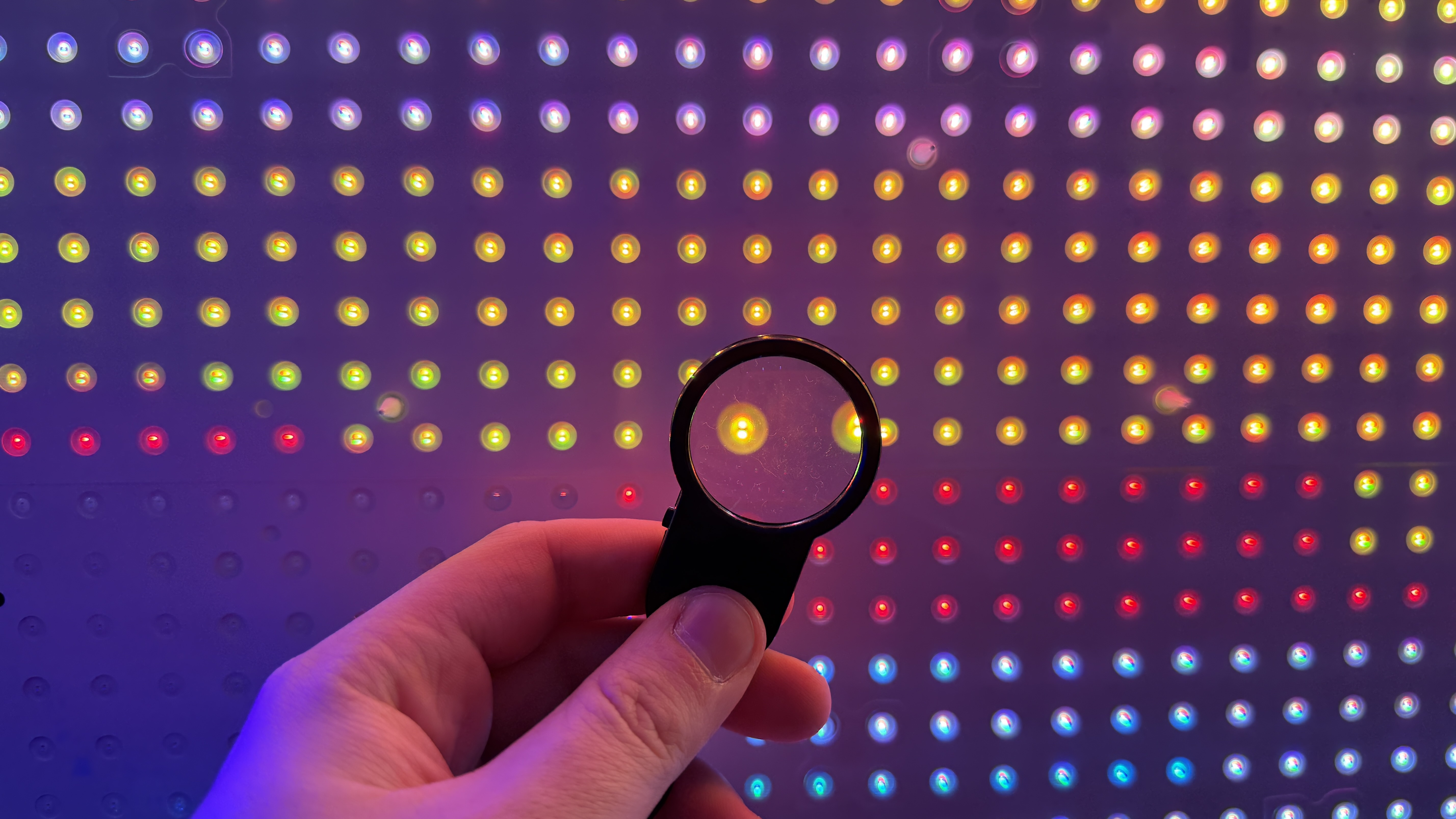 A Sony True RGB TV backlight, with a magnifying glass held up to one LED to show the tech inside it. The pattern of the backlight shows how it shines different colors