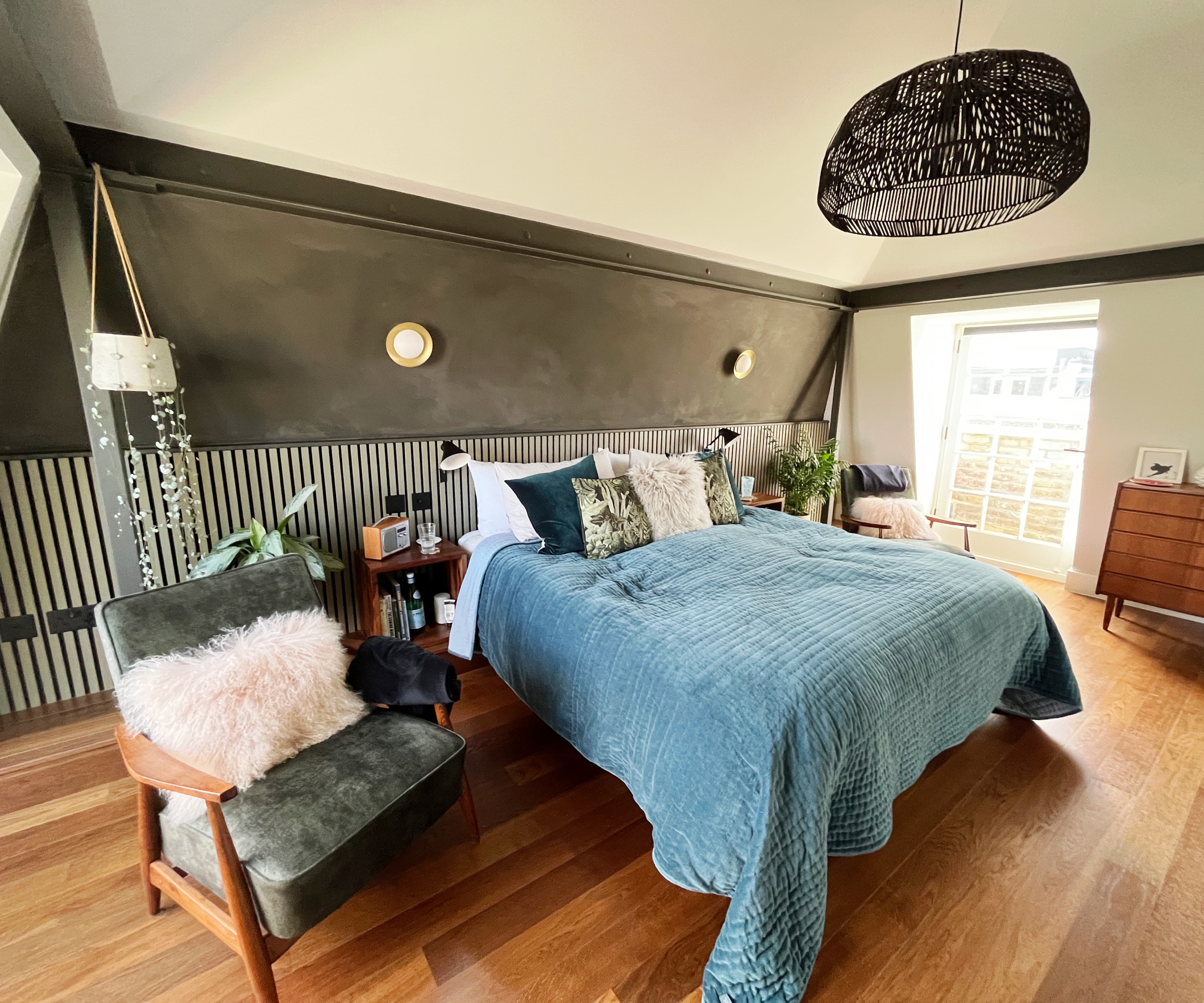 bedroom in mansard loft conversion with white door leading outdoors, wooden floor, dark grey wall with bed, chair and large black pendant shade