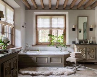 Rustic bathroom with wooden beams, bathtub, stone flooring, sheepskin rug, wall lights