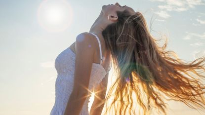 a woman playing with her hair in the sun - summer hair care