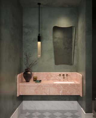 Image of a dark green limewashed bathroom with a light pink marble sink. There is a mirror on the wall and a brown vase on the counter