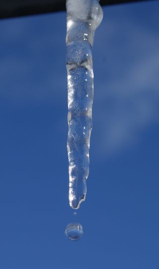 Melting icicle against blue sky.