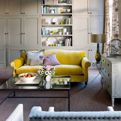 Living room packed with storage and with a glass coffee table and yellow sofa