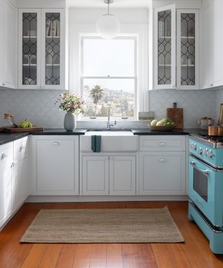 accent colors for a white kitchen, white kitchen with turquoise blue range cooker, scalloped white splash back tiles, rich wood flooring, rug, glazed units, black countertops