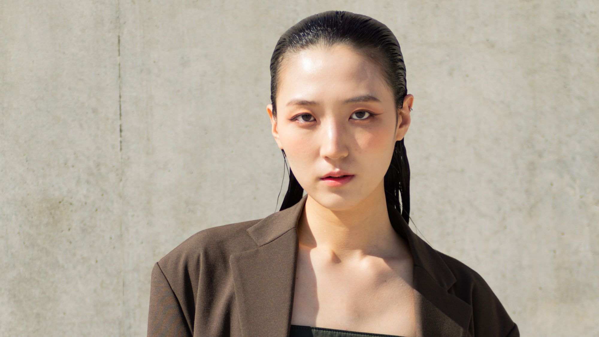 korean model with glowing skin and slicked back hair wearing a brown blazer