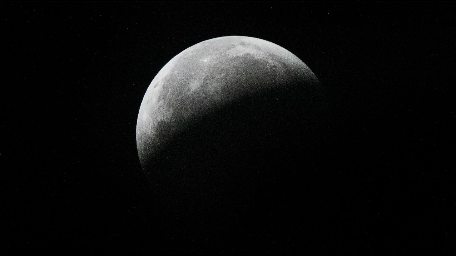 A full moon is pictured against a black sky. It&#039;s lower half is entirely hidden by Earth&#039;s curved shadow and dark basaltic plains called lunar maria can be seen marking the middle of the lunar disk.