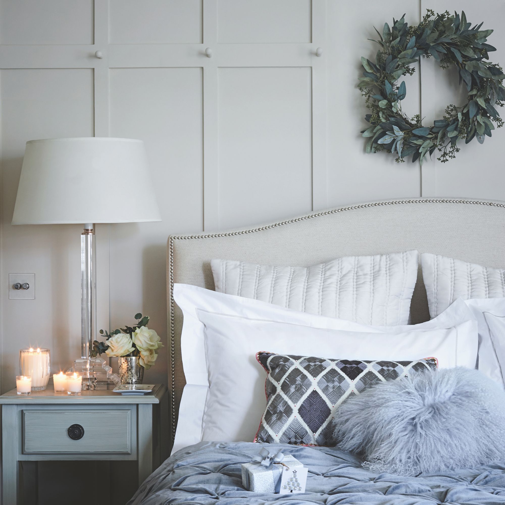 Bedroom with blue and white bedding, a cream headboard and a bedside table with a white lamp on it