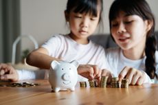 A mother and her daughter putting coins in a piggy bank