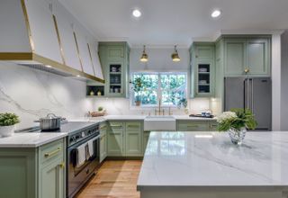 A mint green L-shaped kitchen with brass details and a white marble kitchen island