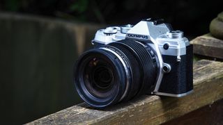 Olympus M.Zuiko 12‑40mm f/2.8 Pro lens on a wooden surface in front of green foliage