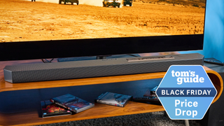 a photograph of the samsung q600f soundbar and subwoofer with a tv in the background playing a desert movie and a tom's guide black friday price drop badge