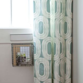 White front door with letterbox cage and blue curtains with white swirls on them in front of the door