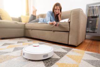 Robot vacuum cleaning room with woman on couch