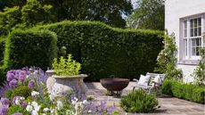 Summer garden patio with firepit and seating, greenery in the background
