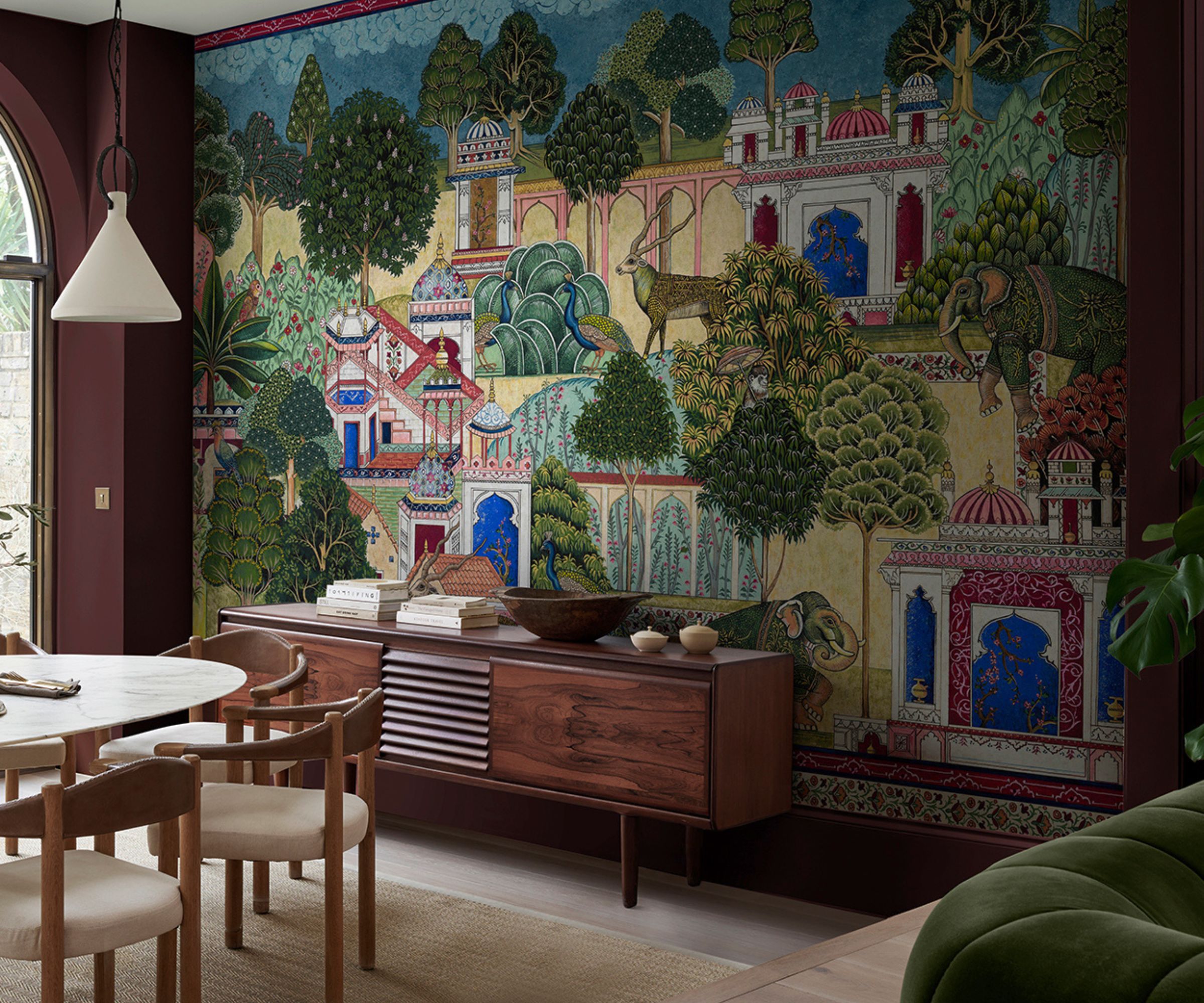 Dining room with burgundy painted wall and large landscape wallpaper mural, wooden console and marble round dining table with wooden chairs