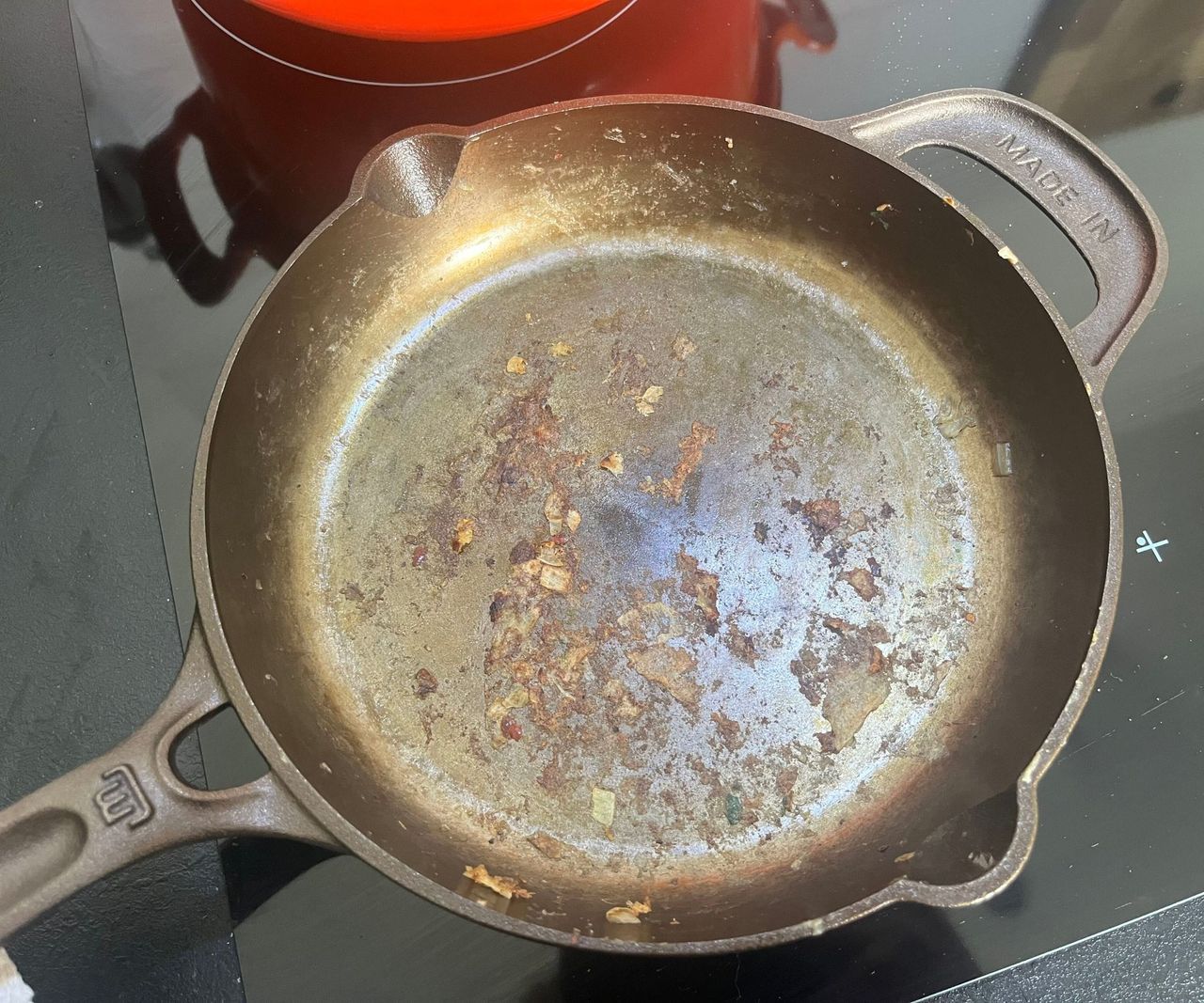 A small bronze colored cast-iron skillet with stuck on pancake residue.