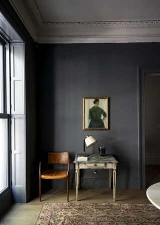 A dark grey blue dining room with framed artwork next to the window