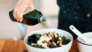 Woman pouring olive oil, one of the best foods for weight loss, onto a salad