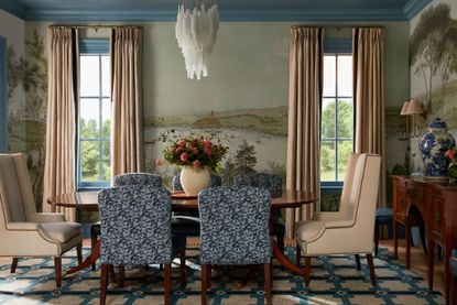 A dining room with a scenic wall mural across the walls, anchored by a patterned rug.