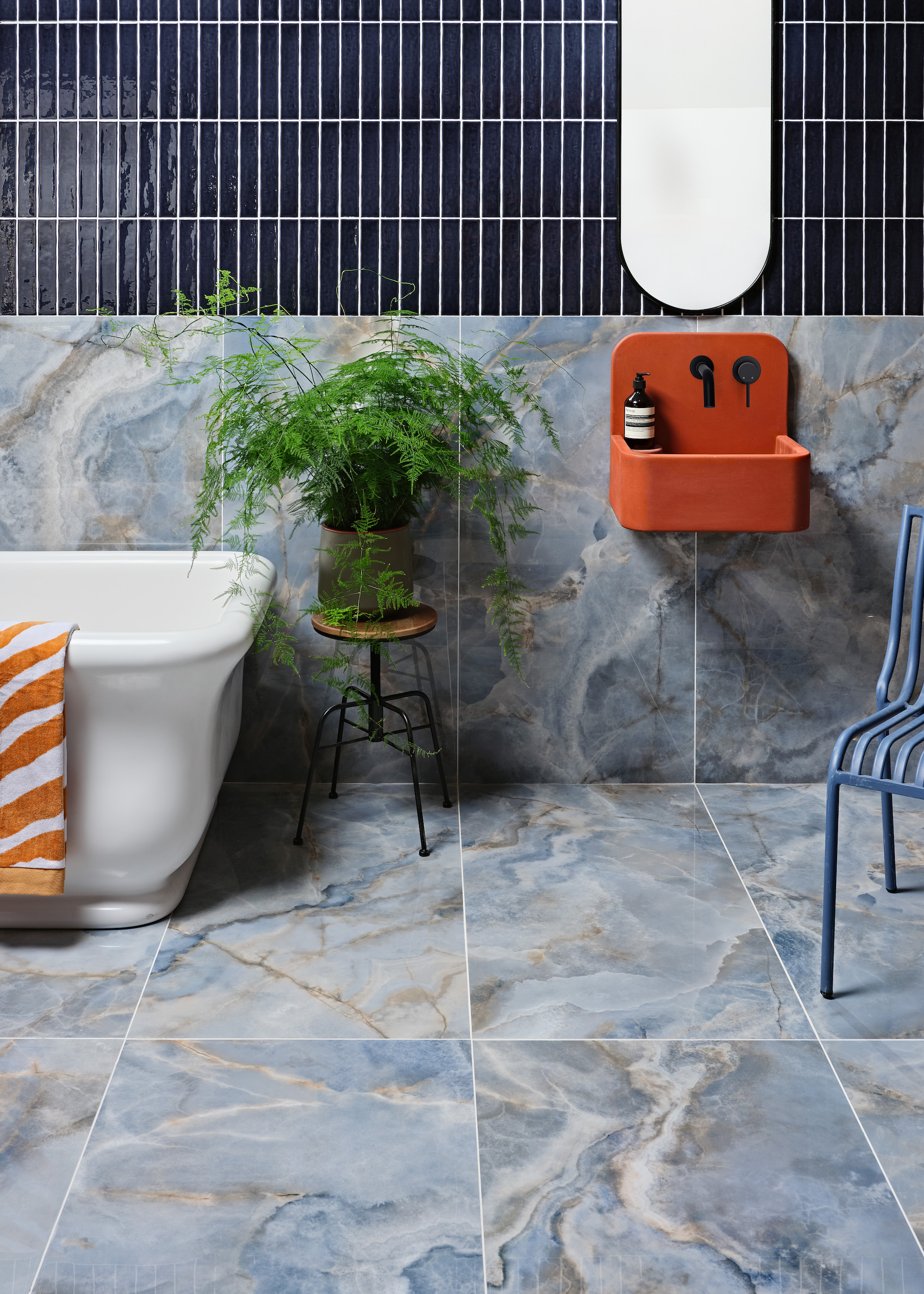 bathroom with onyx tiles and white bath, and orange sink. There is also a small side table with a plant on top of it.