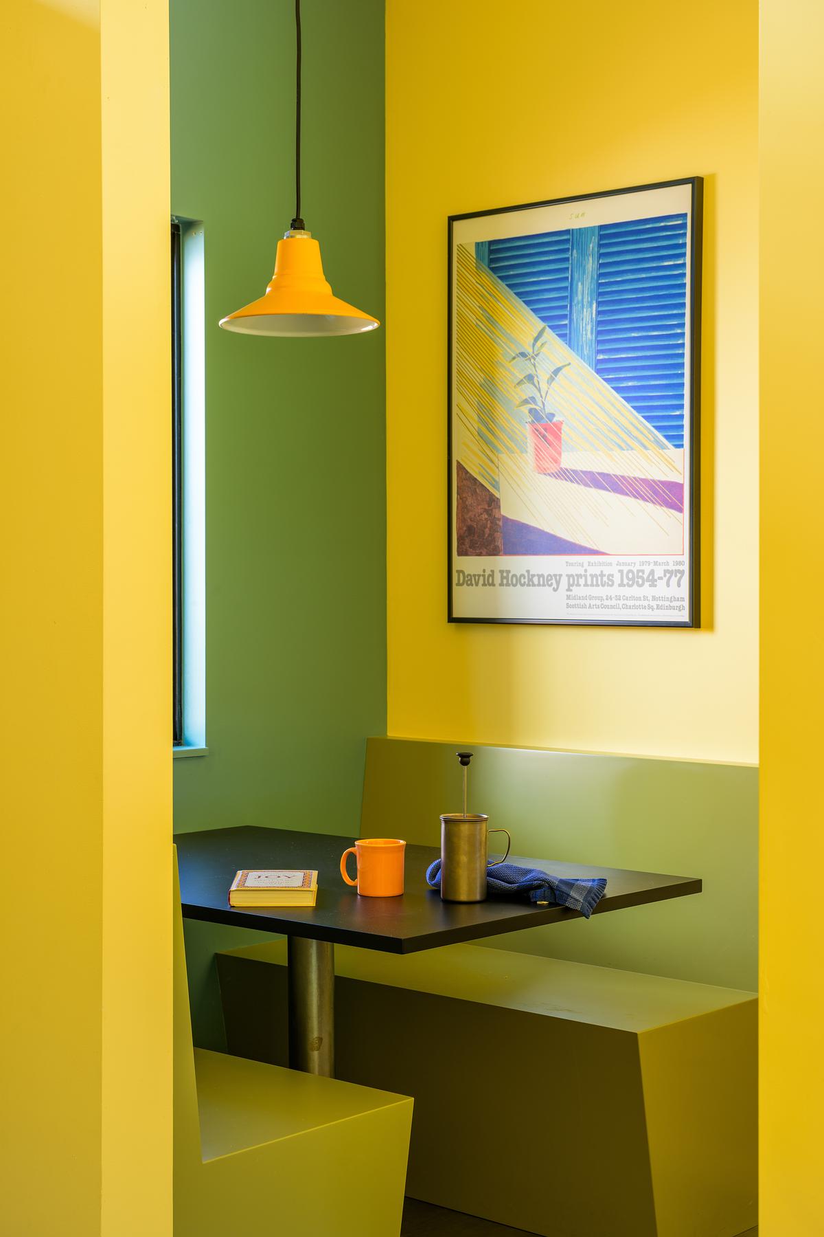 A dining snug painted in a mix of yellow and green with built-in banquette seating, a diner-style table styled with cups, and a large colorful artwork hanging on the wall