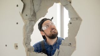 The man looks at the hole he has punched in the wall with a hammer