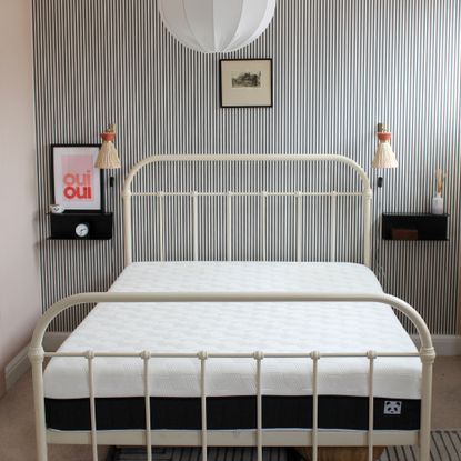 A mattress on a bed with a white bed frame in a room with pink walls and black and white striped feature wall