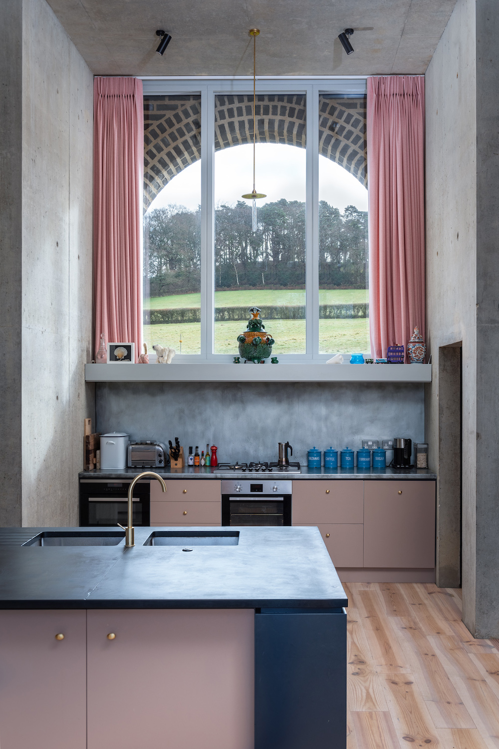 Concrete clad kitchen with pink cabinets and pink curtains