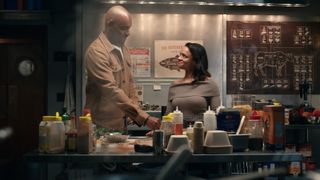 Preacher and Kaia smile at each other behind the counter of a diner in Virgin River season 6.