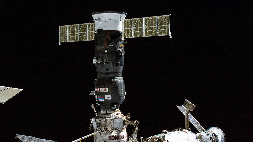 russian progress spacecraft docked with space station. the solar panels are visible and black space is in behind