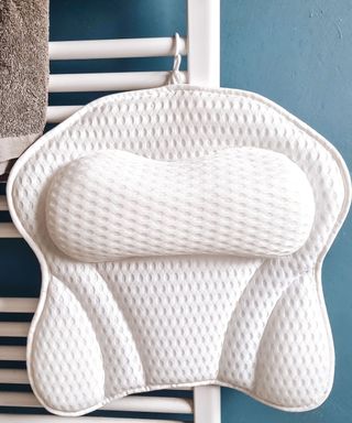 A white mesh butterfly-shaped bath pillow hanging from a white towel rail with a gray towel next to it and a dark blue wall behind it