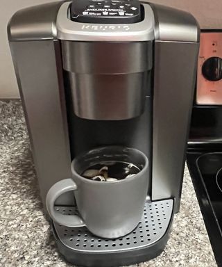 A Keurig K-Elite single-serve coffee maker with prepared iced coffee drink made in grey mug
