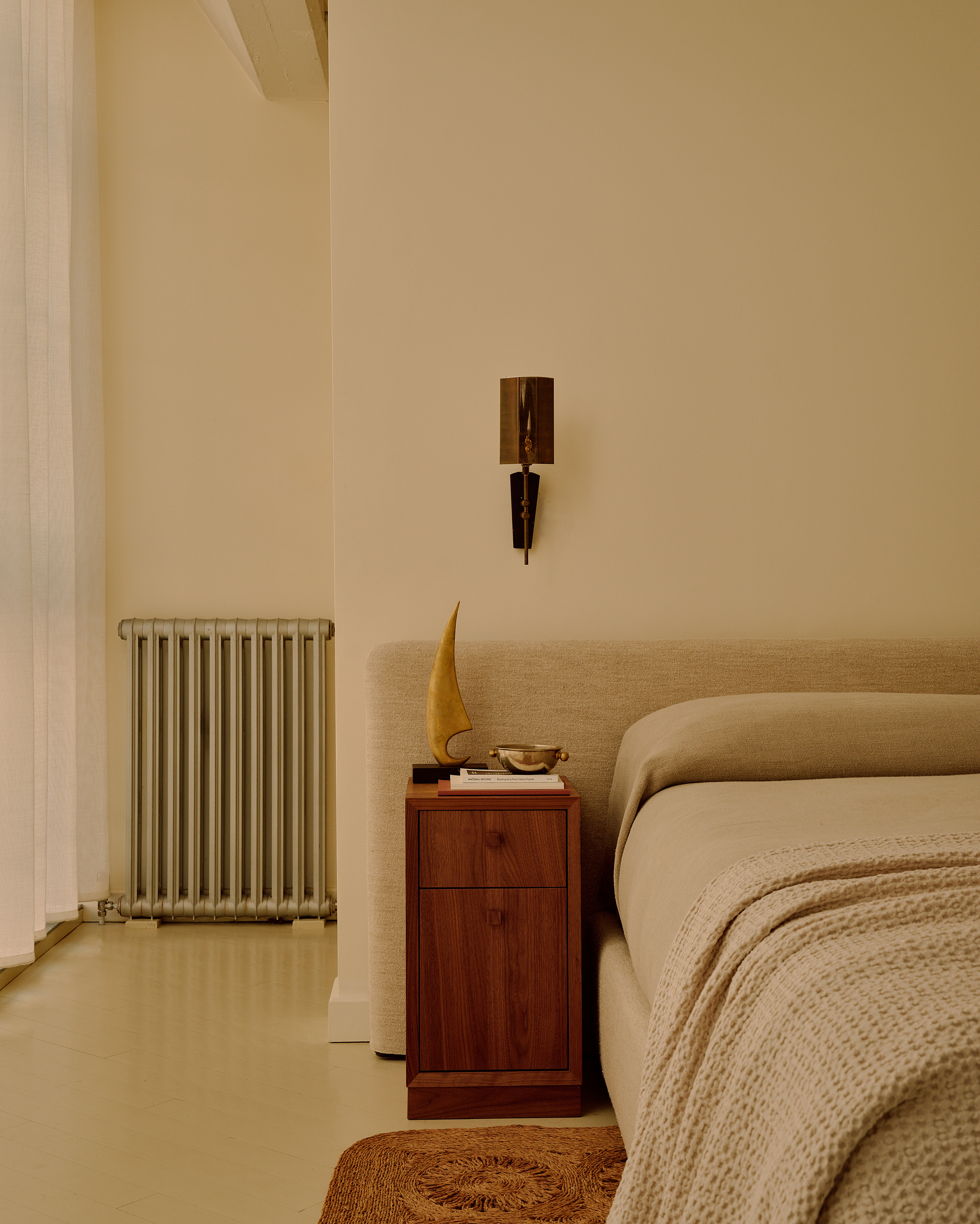 Image of a beige bedroom with a linen headboard, linen bedding, a waffle throw, and linen curtains on the windows.