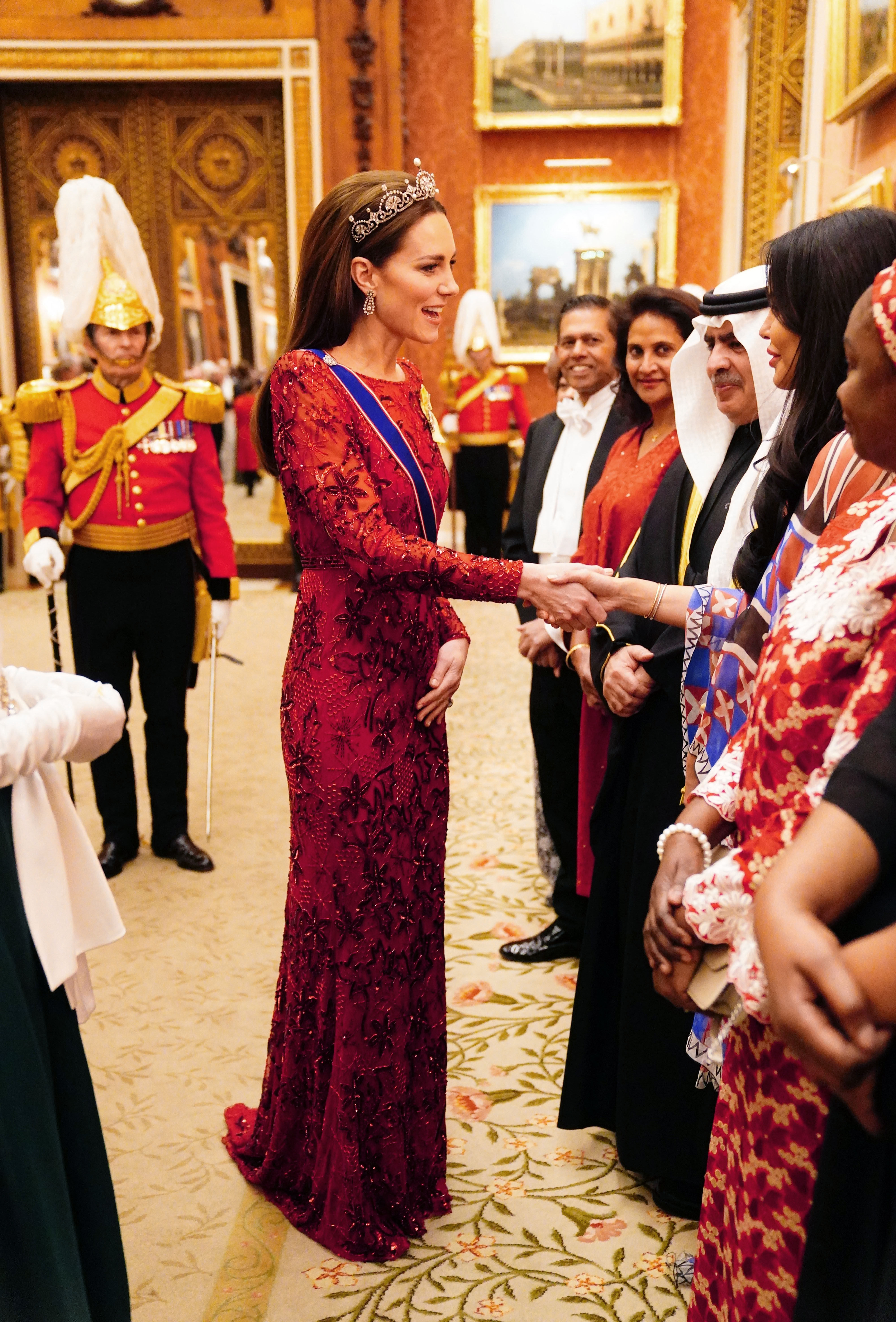 Kate Middleton wearing a red sequin dress and tiara shaking hands
