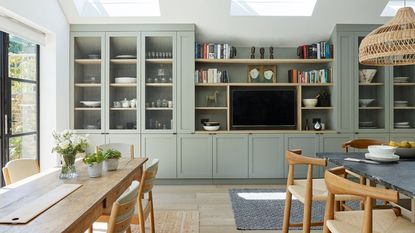 green kitchen and dining area with built in shelves and tv