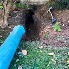 Spade and drainage pipe next to freshly-dug trench in garden