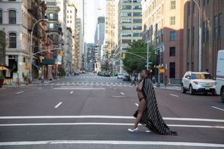 black woman crossing empty road in New York, in white shoes and open robe