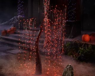 An LED string light tree in front of a haunted house with lights and pumpkins on it