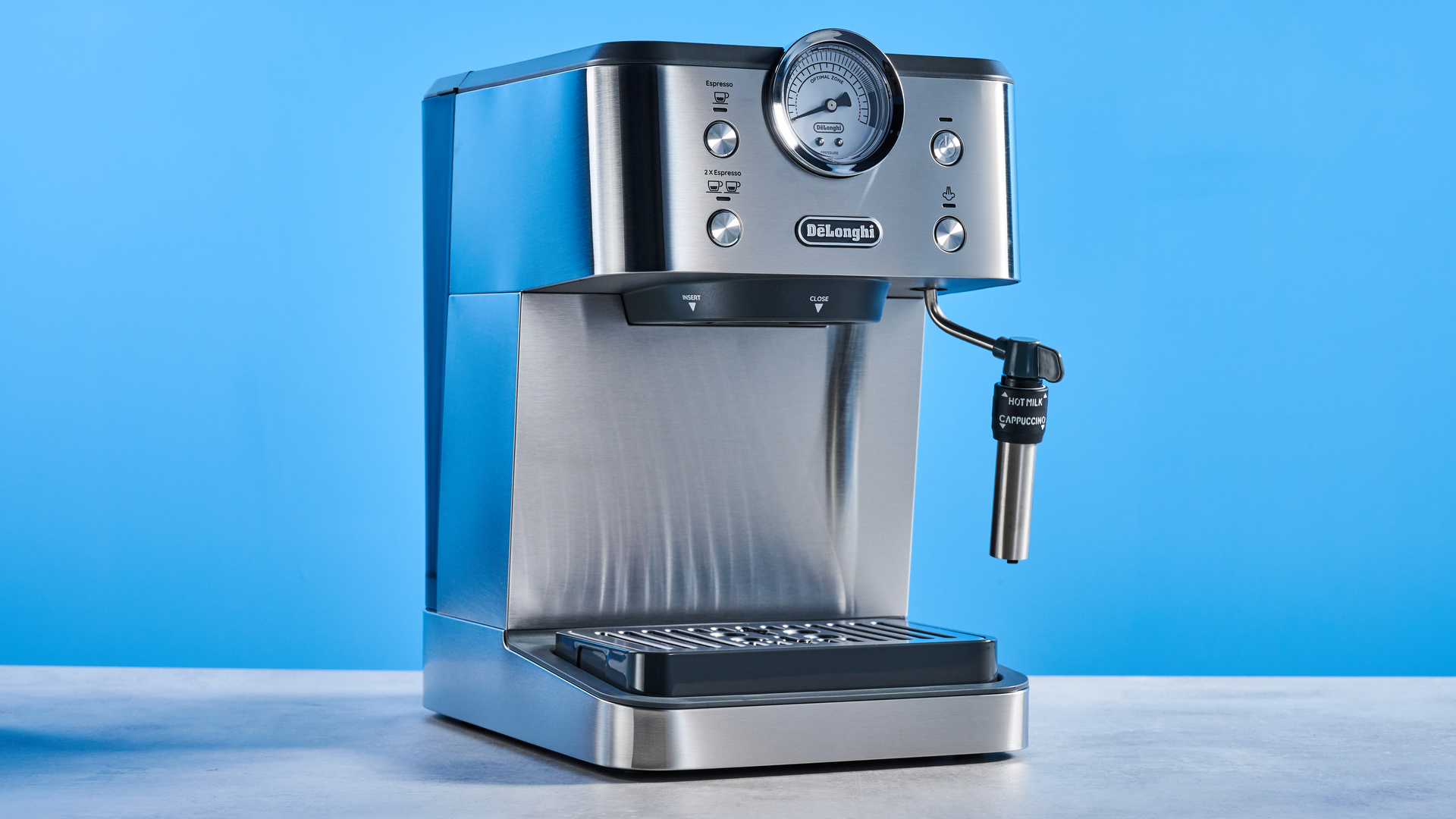 the De'Longhi Linea Classic espresso machine photographed against a blue tom's guide background, showing its silver finish, steam dial, steam wand, portafilter, and accessories