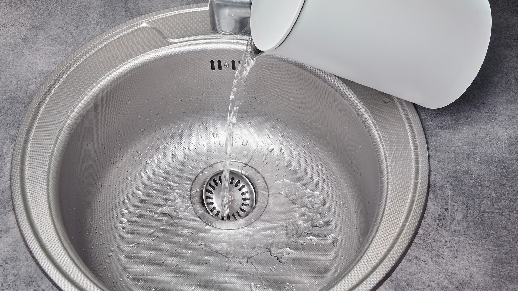 Pouring boiling water from kettle down kitchen sink