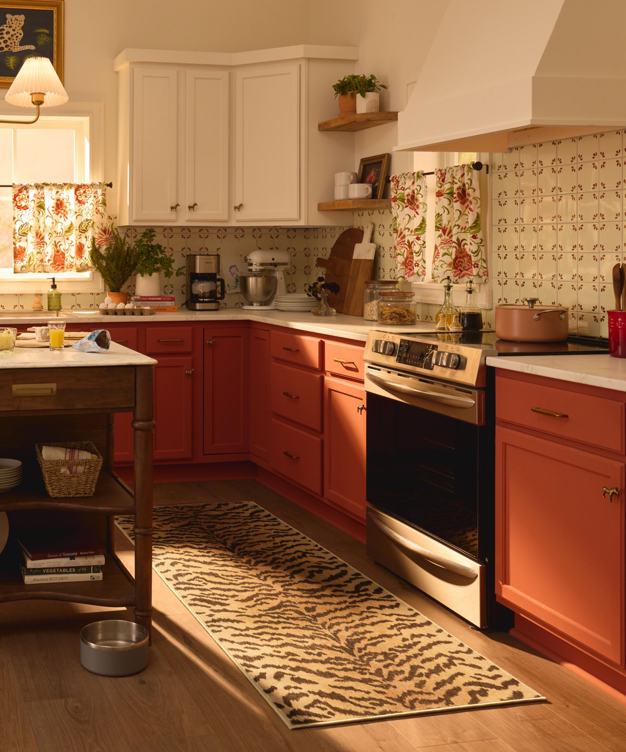 a kitchen with red base cabinets, white upper cabinets, countertops with decor on top, and a tiger printed runner rug