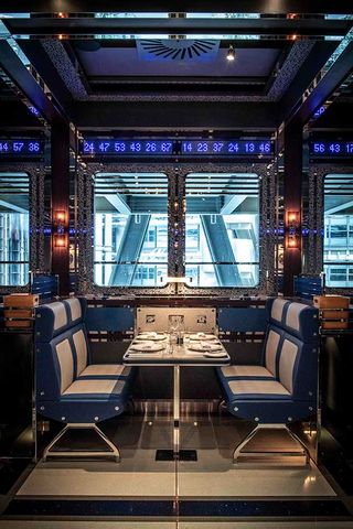 Dining booth at Bob Bob Cité restaurant with a decorated table, white and blue chairs, a window, wall lights and a strip of blue glowing numbers running below the ceiling.