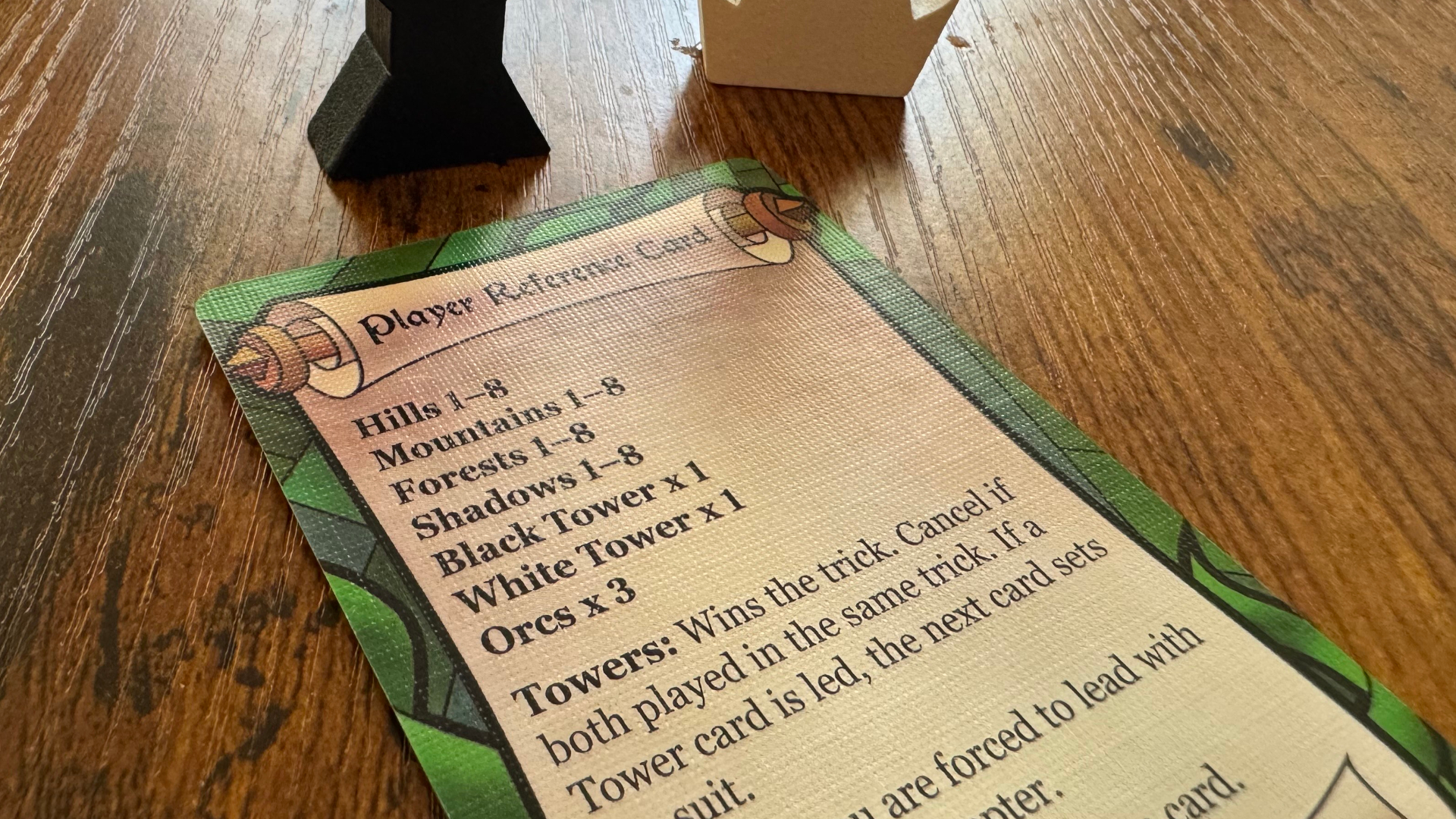 A player reference card from Two Towers Trick-Taking Game laid out on a wooden table