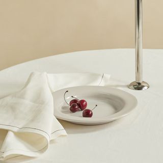 A white dinner plate with some cherries on it on a white table cloth