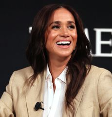 Meghan Markle wearing a beige linen suit and white shirt on stage at Time100 Summit