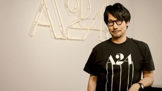 Hideo Kojima poses in front of an A24 logo with a black t-shirt on
